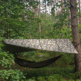 Bushmen Thermo Tarp 2×3 camouflage tarp setup in a wooded area, providing shelter over a hammock.